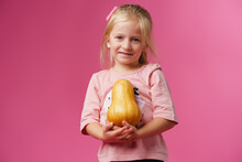 Little Girl Holding Pumpkin In Her Hands Against Pink Background