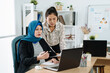 © PR Image Factory - Casual pregnant businesswoman in suit and headscarf working with colleague in office. young maternity muslim lady worker using laptop computer at desk and talking to coworker. teamwork solve problem.