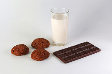 A glass of milk, a bar of chocolate, and three oatmeal cookies. Isolate on a gray background with shadows.