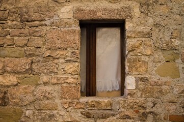 Wall Mural - An isolated window with white curtains partially hidden by the stone wall of an abandoned medieval building (Gubbio, Umbria, Italy, Europe)