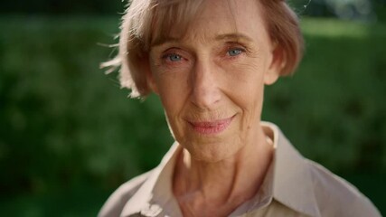 smiling senior woman posing at camera in summer garden. senior lady looking down