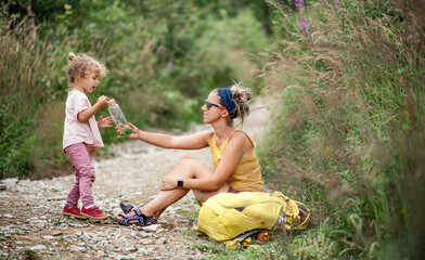 Wall Mural - mother with small toddler daughter hiking outdoors in summer nature, resting.