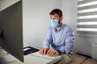 © Dusan Petkovic - Dedicated young attractive businessman with protective mask on sitting in office and typing report.