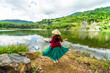 © CravenA - Vietnamese girl in dark red and bottle green traditional costume dress with conical hat standing in front of Ba Be lake
