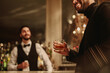 © Jacob Lund - Young man holding glass of whiskey at bar counter with bartender in background in nightclub