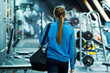Fit woman in sportswear entering gym, blurred equipment. Young female preparing for training. Concept of fitness