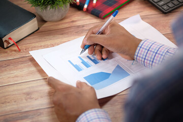 rear view of man's hand with pen analyzing bar chart on paper 