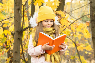 Wall Mural - A little girl reads a book in the woods in autumn.