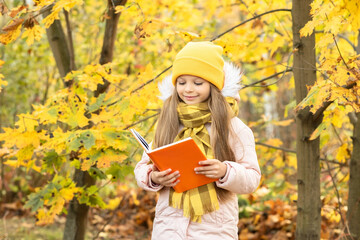 Wall Mural - A little girl reads a book in the woods in autumn.