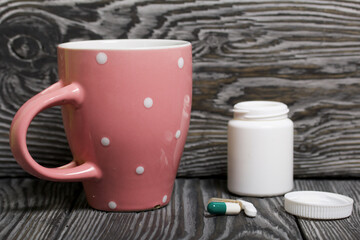 Wall Mural - Container with pills and a mug of water. The lid of the container and several tablets are next to each other. On pine planks in black.