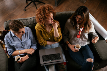 Wall Mural - Girlfriends talking and laughing in office. Beautiful women drinking coffee in the office.