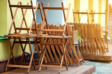 Wooden furniture folded on summer terrace before the opening of the restaurant. Street cafe before opening. Pile of wooden chairs and tables on summer terrace of street cafe.