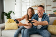 © JustLife - Husband and wife playing video game with joysticks in living room. Loving couple are playing video games at home.