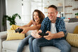 © JustLife - Husband and wife playing video game with joysticks in living room. Loving couple are playing video games at home.