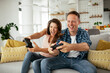 © JustLife - Husband and wife playing video game with joysticks in living room. Loving couple are playing video games at home.