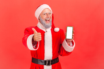 Wall Mural - happy satisfied man with gray beard in santa claus costume holding smartphone with empty white displ