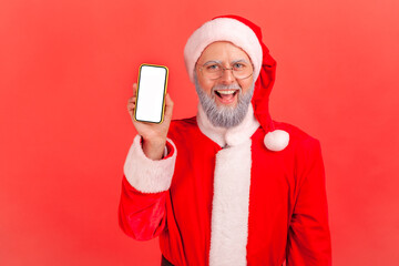 Wall Mural - happy gray bearded santa claus holding and showing smartphone with white display looking at camera w