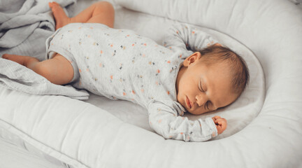 newborn baby sleeping in safe in her bed on a white blanket at home