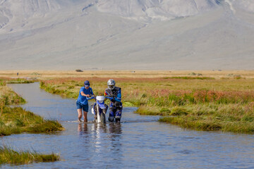 Two men are pushing a motorcycle along a road flooded with water. Altai, Mongolia.