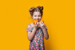 © Strelciuc - Charming blonde girl tasting sliced oranges posing in a dress on a yellow studio wall