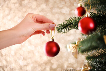 female hand decorating christmas fir tree on blurred lights background