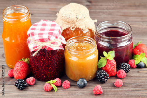 Sweet jam in glass jars with berries on wooden table