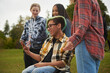© Dann - Disabled teenage boy on wheelchair with his friends looking at smartphone in forest