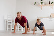 © Елена Лавринович - Father and son play sports in the bright kitchen at home. Home workouts. Stay home. Family concept. A man and a boy are doing push-ups.