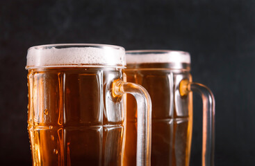 2 mugs of light beer with foam on a dark wooden background,