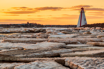 Wall Mural - Frozen sea with large ice blocks sheets against a red and white lighthouse during sunset in Charlottetown Prince Edward Island, Canada