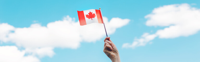 Wall Mural - Closeup of woman human hand arm waving Canadian flag against blue sky. Proud citizen man celebrating national Canada Day on 1st of July outdoors. Web banner header.