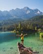 Girl in yellow standing on a rock, spreading arms and watching a beautiful view over lake Eibsee in the Bavarian Alps