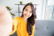 Pretty Young Asian Female With Big Smile Sitting At Living Room. She Having Fun Taking Light Cheerful Selfie On Blurred Background