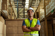 © twinsterphoto - Portrait of young Indian industrial worker with arm folded working in logistic industry indoor inside factory warehouse. Smiling happy man in hard hat looking at camera arms crossed at depot