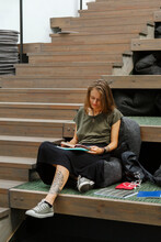 Trendy Young Woman Reading Book While Sitting Alone And Waiting Lecture In Modern Auditorium Of University