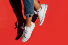 Close-up Of Of Female Wearing Sneakers While Jumping Against Red Background