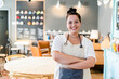 © Giorgio Fochesato/Westend61 - Smiling female owner with arms crossed standing against furniture in coffee shop