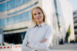 © Joseffson/Westend61 - Beautiful blond female entrepreneur smiling while standing with arms crossed at financial district