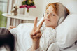 © Mareen Fischinger/Westend61 - Sick boy lying in hospital making victory sign, wearing head phones