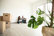 © MiJo/Westend61 - Man sitting with wife using laptop on hardwood floor in new unfurnished house