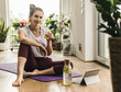 © UWE_UMSTAETTER/Westend61 - Young woman holding drink while sitting on exercise mat at home