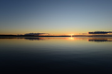 Wall Mural - Sunset on the horizon over a calm water surface lake