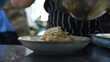 Bustle In The Restaurant Kitchen On A Weekend. The Chef Lays Out The Fried Squid Ring From Metal Bowl On A Plate With Tweezers. Working Atmosphere, Dishes From The Menu Are Prepared On The Back Pallet