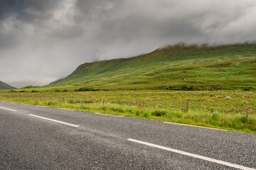 Narrow empty asphalt road into mountains, Low cloudy sky over peaks. Nobody, Connemara, Ireland. Concept travel, road trip