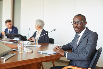 Wall Mural - portrait of african leader looking at camera while sitting at the table with business people at boar
