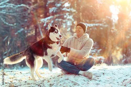 Cuadros en Lienzo young man hugs a husky dog in the winter in the forest, a man and a dog hug toge