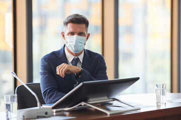 Wall Mural - portrait of mature businessman in protective mask looking at camera while sitting at conference