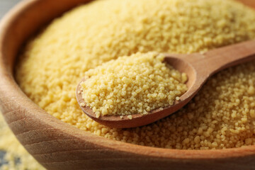 Bowl with couscous and spoon on wooden background