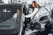 © fotofabrika - Young attractive woman salesperson in car showroom showing a car to her male client