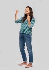 success, winning gesture and people concept - happy young asian woman celebrating victory over grey background